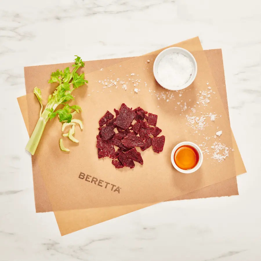 Portioned packages of Beretta Original Beef Jerky on a paper, with ingredients like celery and salt visible.
