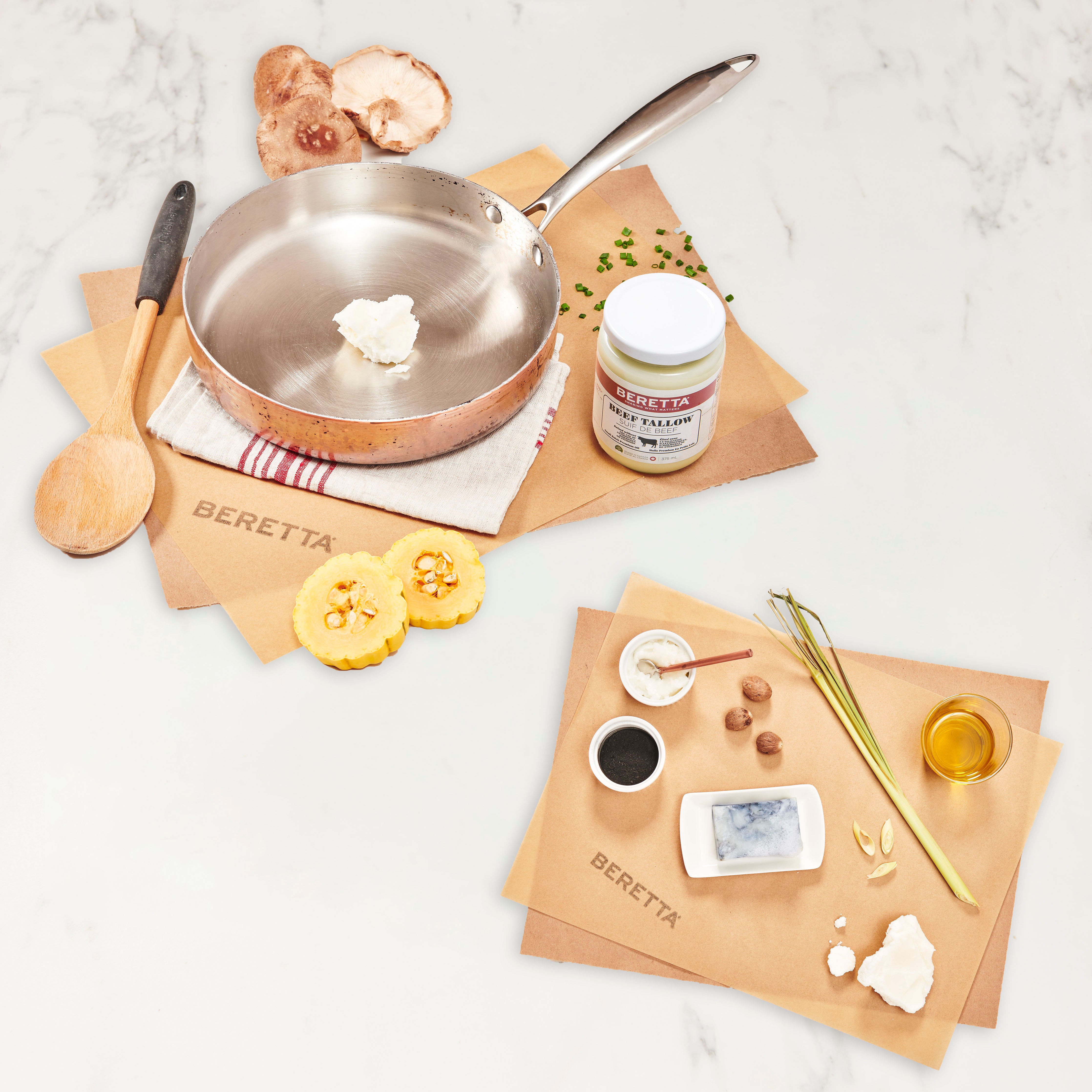 A bundle setup with a jar labeled 'Tallow', a copper pan, wooden spoon, charcoal soap bar, and various other kitchen-related items on a marble surface.